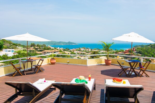 A terrace with wooden furniture, white umbrellas, and a view of the sea and hills. - Pousada e Spa Villa Mercedes by Latitud Hoteles (Búzios)