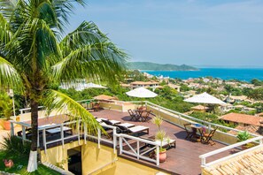 A rooftop terrace with lounge chairs, umbrellas, and a view of the sea and surrounding buildings. - Pousada e Spa Villa Mercedes by Latitud Hoteles (Búzios)