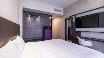 Une chambre d’hôtel moderne dotée d’un grand lit, d’un téléviseur fixé au mur, d’une armoire et d’un coin salon avec un fauteuil.