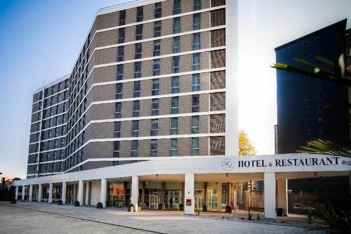 Un hotel moderno con estructura de varios pisos, grandes ventanales y un área de acceso techada.