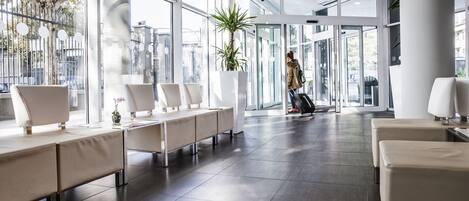 Eine moderne Hotelhalle mit großzügigem Raumangebot, großen Fenstern und einer zentral platzierten Pflanze.