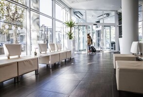 Un'accogliente hall di un hotel moderno, con ampi spazi, grandi finestre e una pianta al centro.