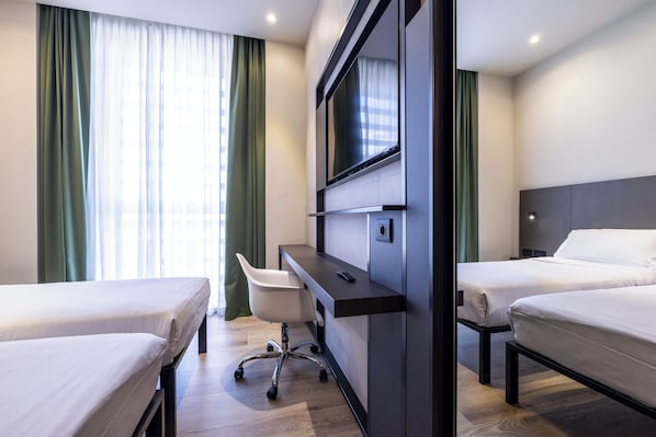 Habitación de hotel con dos camas, un escritorio con silla, televisor montado en la pared y ventana con cortinas.