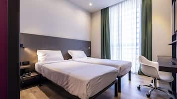 Habitación de hotel con dos camas individuales, un escritorio y una silla.