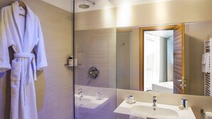 A bathroom with a glass shower enclosure, a sink with a mirror, and a robe hanging on a rack. - Hotel Degli Arcimboldi (Milan)