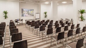 Un salón de conferencias con filas de sillas, una pizarra y un ordenador portátil sobre una mesa.