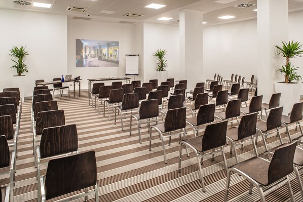 Un salón de conferencias con filas de sillas, una pizarra y un ordenador portátil sobre una mesa.