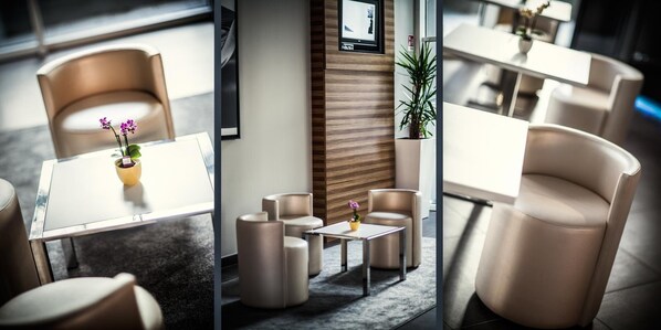 Un moderno vestíbulo de hotel con una zona de estar que incluye mesas y sillas redondas, una pared decorativa de madera y una planta en maceta.