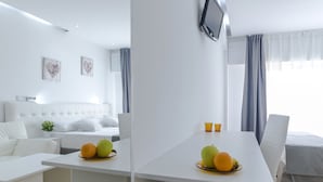 Uma sala de estar moderna e minimalista com um sofá branco, uma mesa de jantar com frutas e uma janela grande com cortinas.