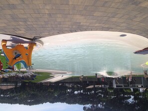Parque acuático interior con una piscina de olas grande, toboganes y una zona de juegos.