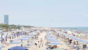 Une plage bordée de rangées de parasols et de chaises longues, un ciel dégagé et une vue lointaine sur la mer.