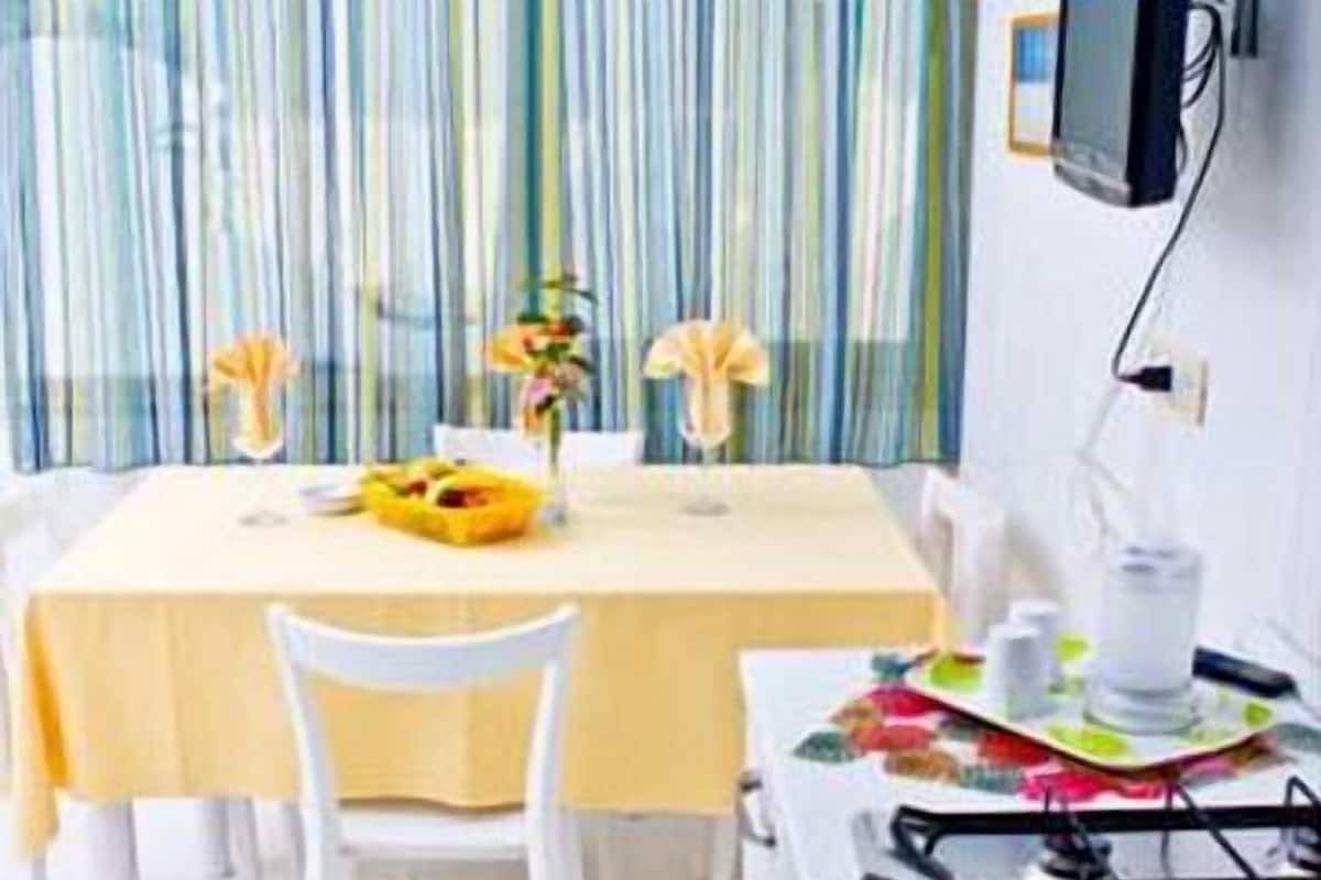 Un coin repas avec une table dressée pour deux personnes, une cuisinière à gaz et un téléviseur fixé au mur.