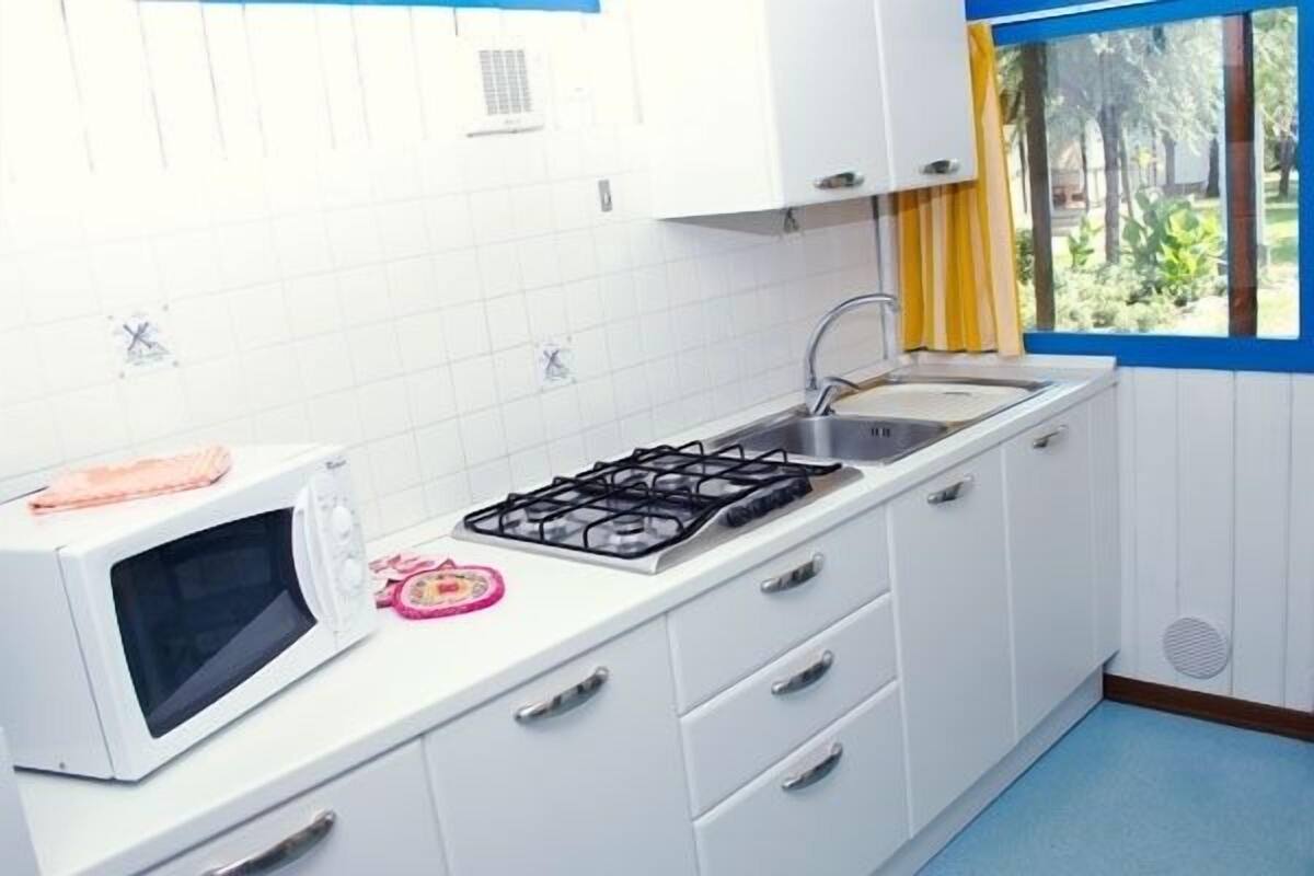 Une cuisine avec des meubles blancs, une cuisinière à gaz, un four à micro-ondes, un évier et une fenêtre donnant sur un paysage verdoyant.