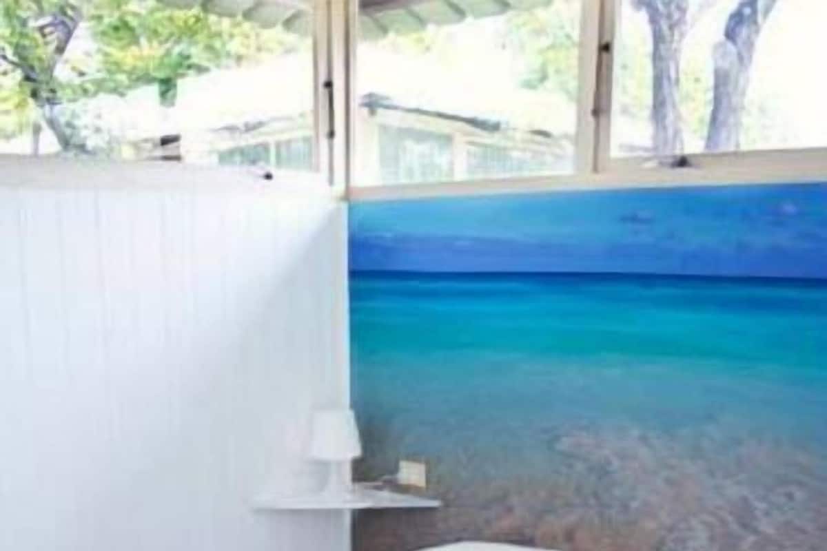 Une chambre à coucher avec un lit, une table de chevet et une fresque murale représentant une scène de plage.