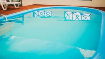 An indoor swimming pool with a blue interior, a ladder, and patterned cushions.