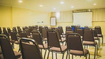 Uma sala de conferências com fileiras de cadeiras, uma tela de projeção e um quadro branco.