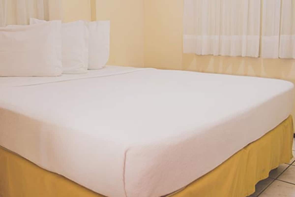 Ein Bett mit gelbem Bettrunden, weißen Kissen und einer weißen Decke.
