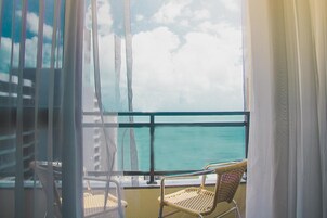 Un balcone con vista sul mare, una sedia in vimini e una sedia bianca.