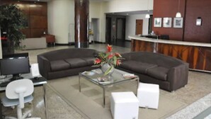 Een moderne lobby met een gebogen, donkerbruine bank, een glazen salontafel met een bloevas, een receptiebalie en een witte bureaustoel.