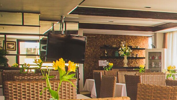 Een ruime hotellobby met rieten meubilair, een bar en grote ramen voorzien van gordijnen.