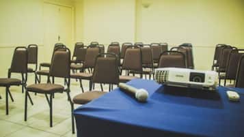 Uma sala de conferência com fileiras de cadeiras, uma mesa com projetor e um microfone.