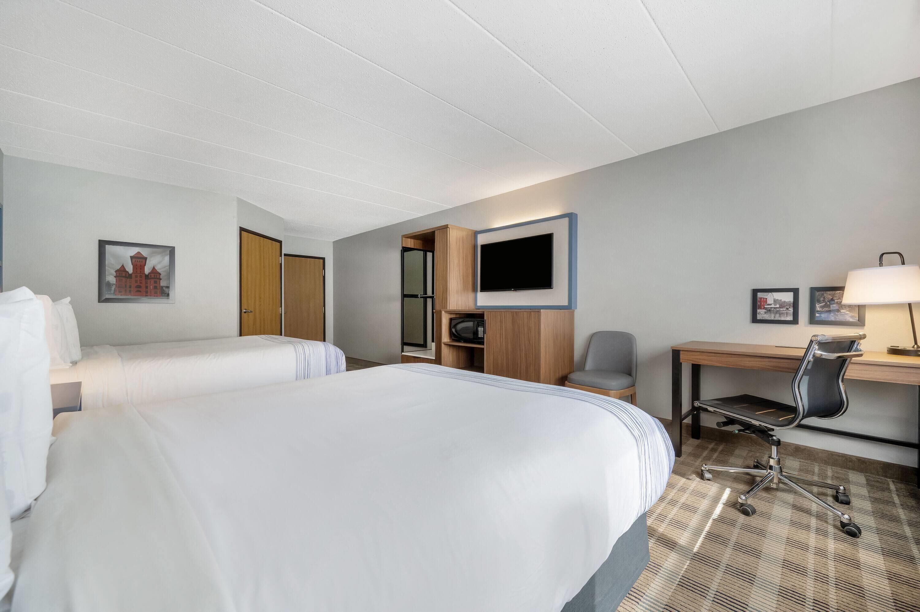 A hotel room with two beds, a desk with a chair, a television, and a small cabinet.