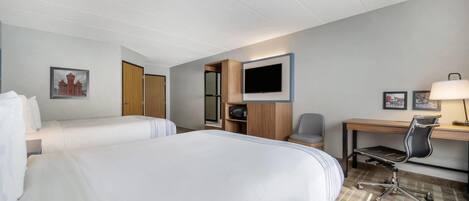 Une chambre d’hôtel avec deux lits, un bureau avec une chaise, une télévision et un petit placard.