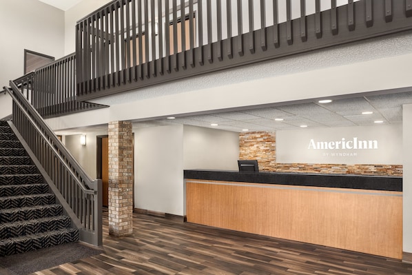 A hotel reception area with a reception desk, a staircase, and a stone pillar.
