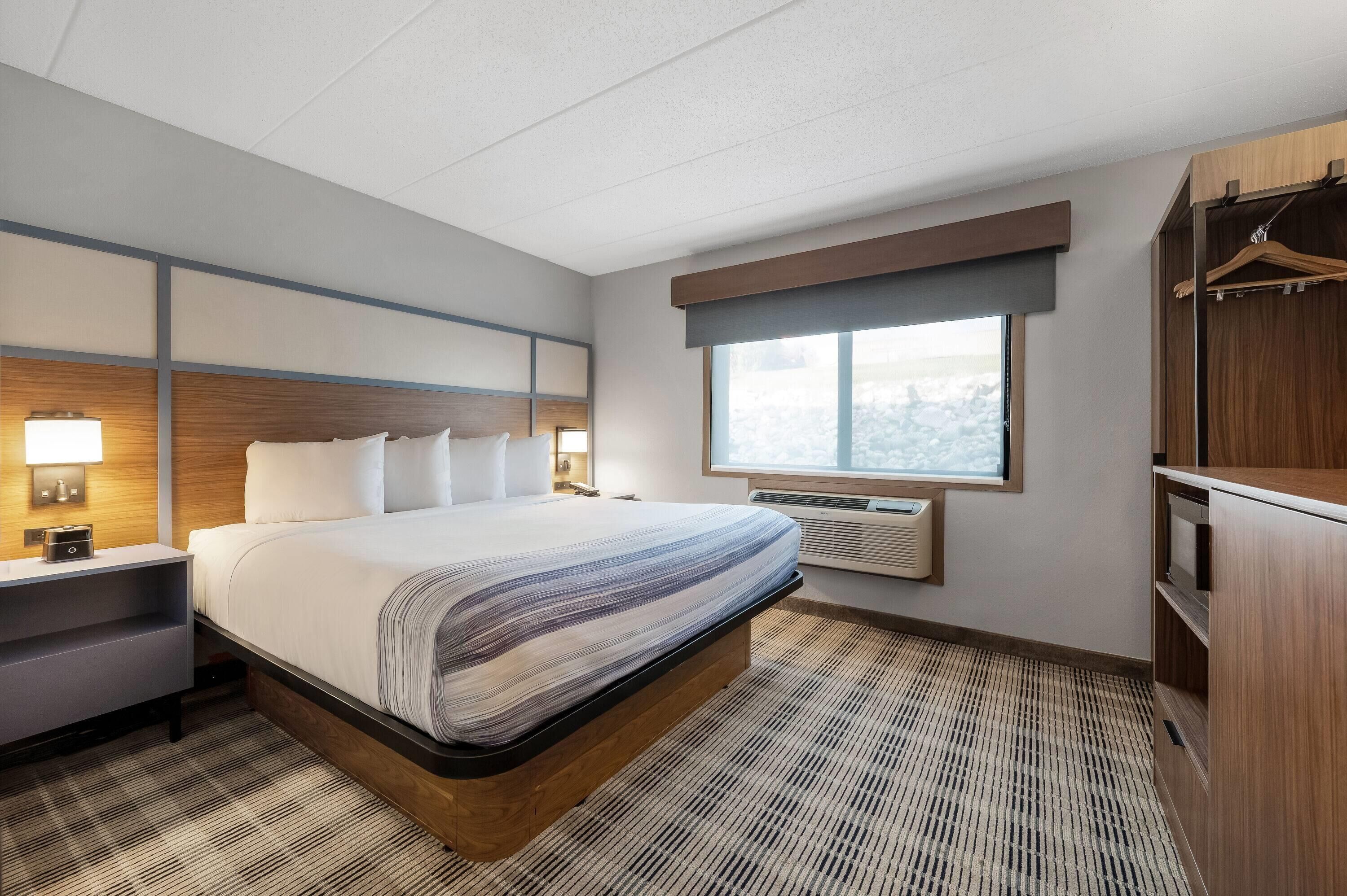 Habitación de hotel con cama, mesitas de noche, escritorio, armario, ventana con vistas y equipo de aire acondicionado.