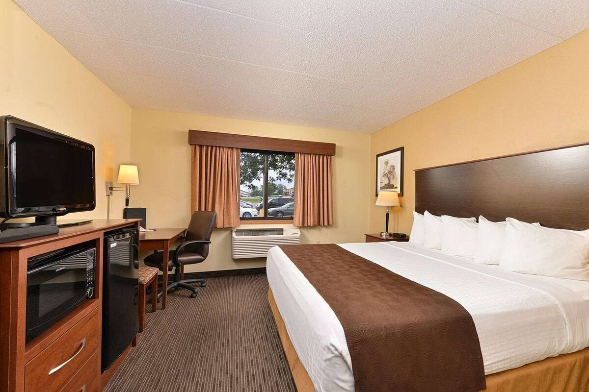 Habitación de hotel con cama, escritorio con televisor, microondas, silla y ventana con cortinas.