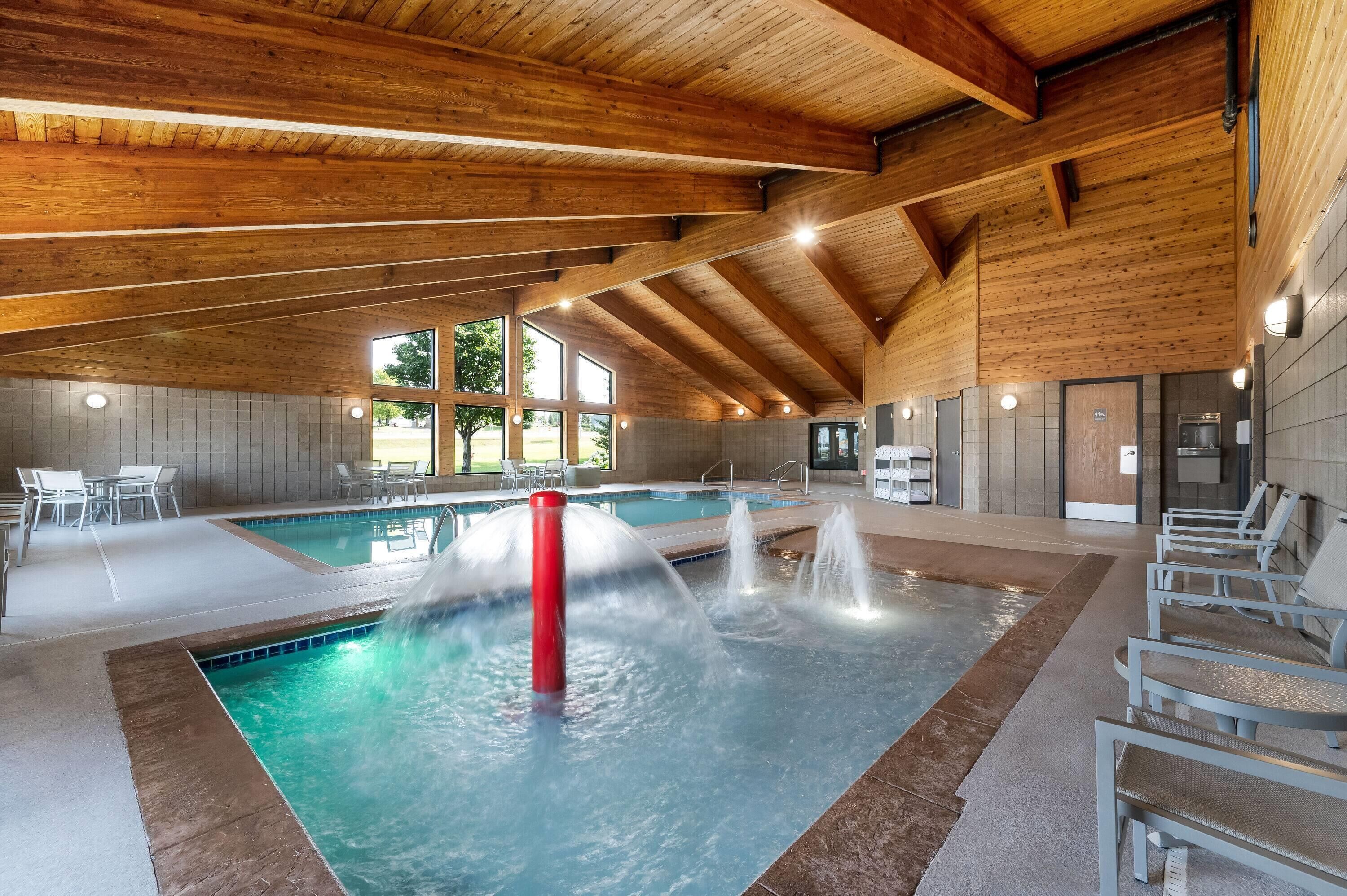 Una piscina interior con una fuente de agua, vigas de madera en el techo y zonas de estar.