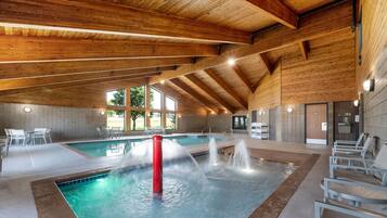 Una piscina interior con una fuente de agua, vigas de madera en el techo y zonas de estar.
