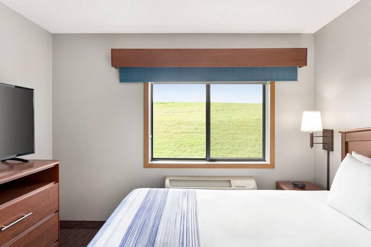 Habitación de hotel con cama, televisión, escritorio, lámpara y ventana con vista a un campo verde.