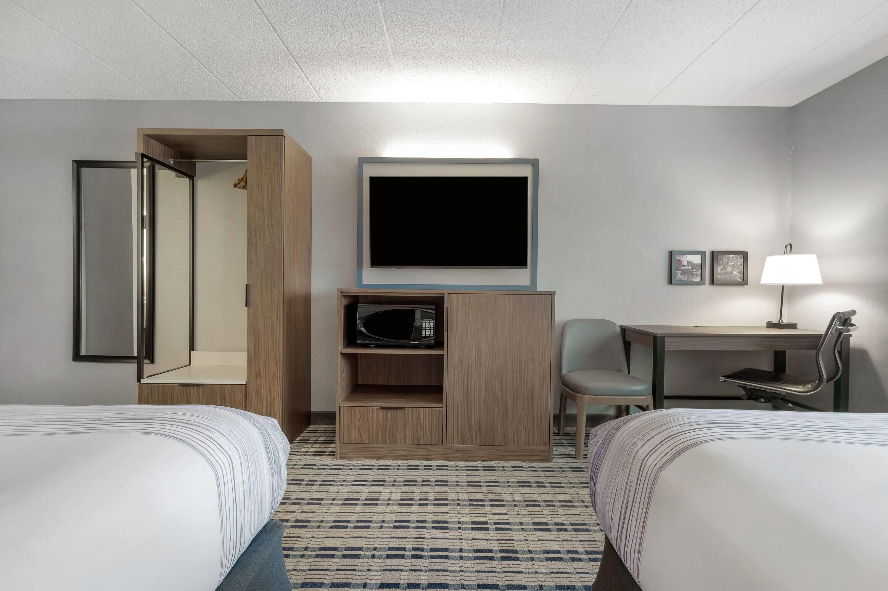 A hotel room with two beds, a TV, a microwave, a desk with a chair, and a lamp.
