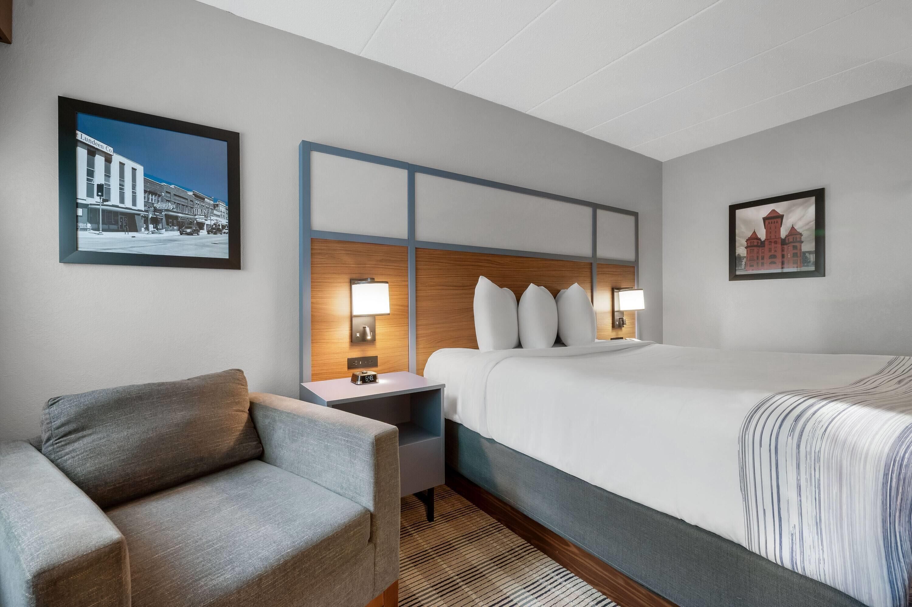 Une chambre d’hôtel comprenant un lit, une chaise, une table de chevet et deux lampes fixées au mur.