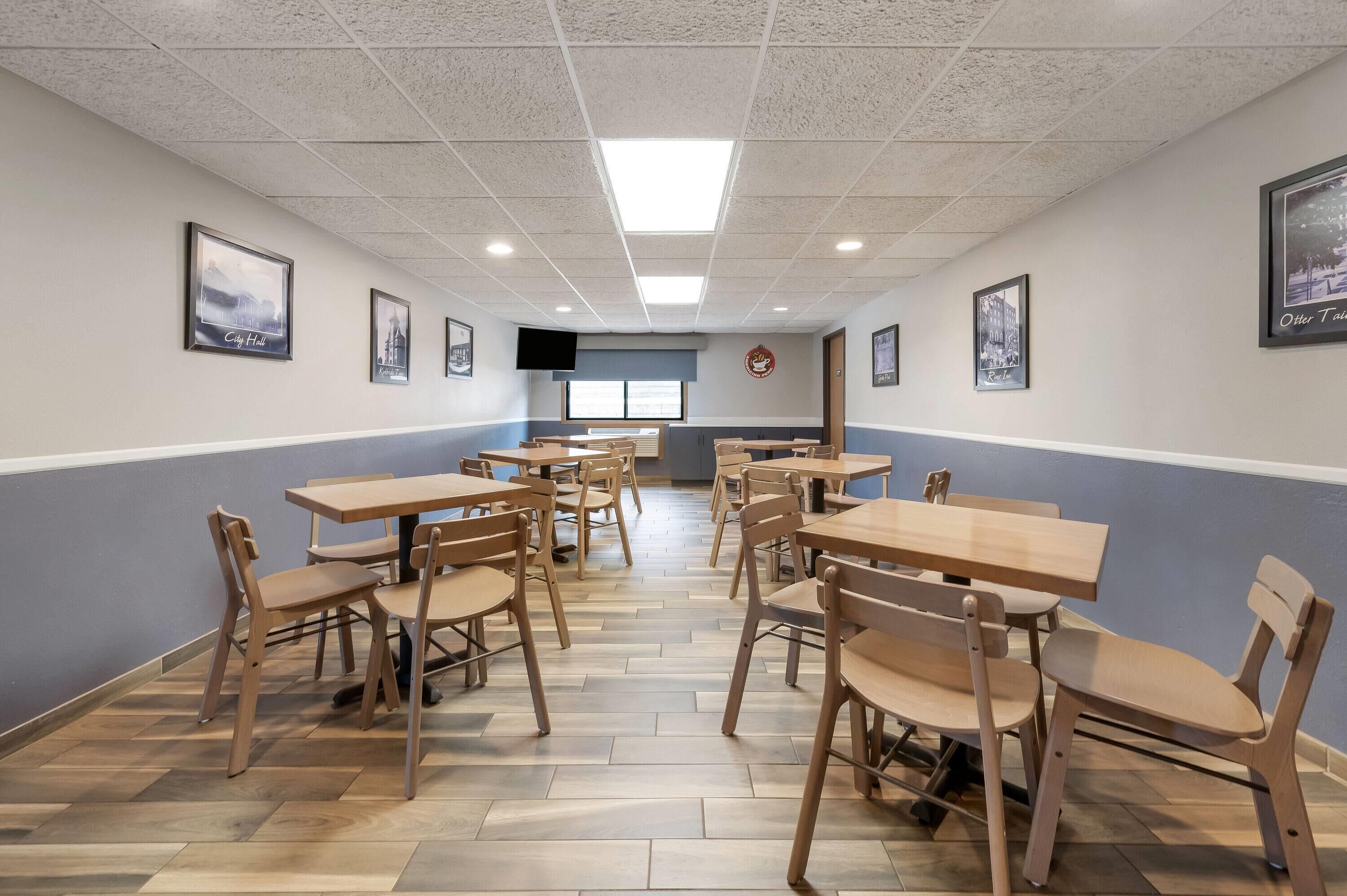 A dining area with wooden tables and chairs, a tiled floor, and framed pictures on the walls.
