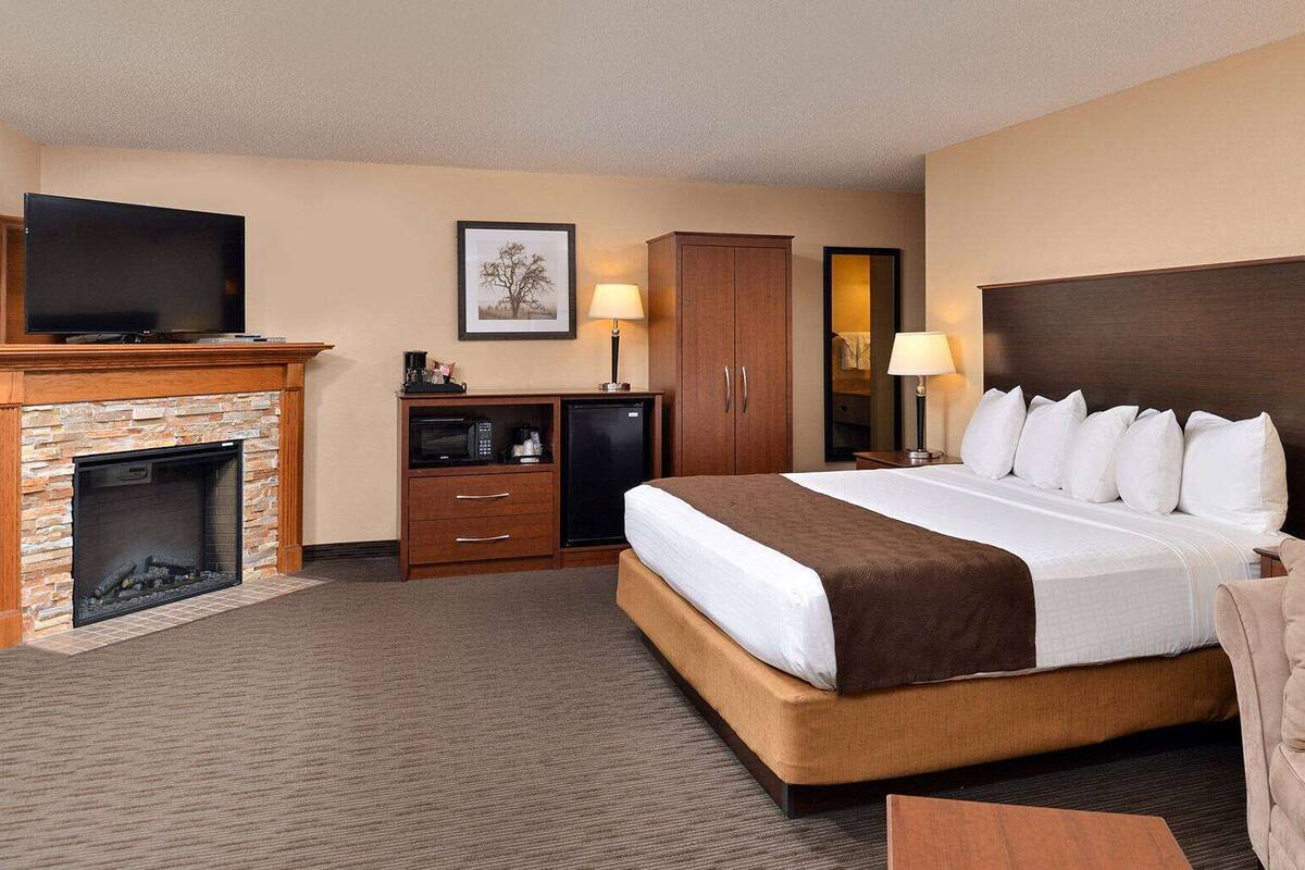 Una habitación de hotel con una cama grande, chimenea, televisor, escritorio y armario.