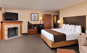 A hotel room with a large bed, a fireplace, a television, a desk, and a wardrobe.