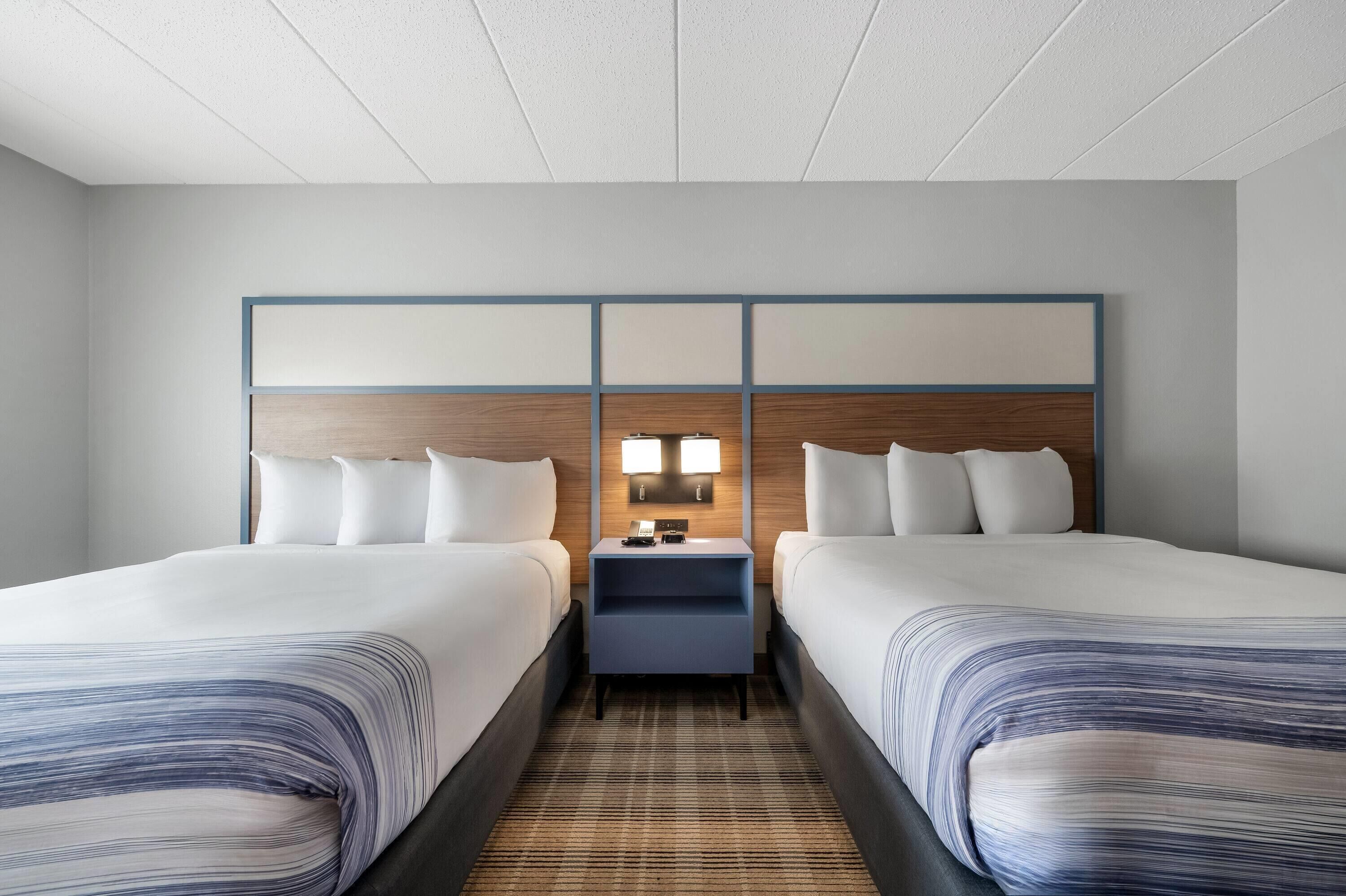 A hotel room with two beds, a nightstand with a lamp, and a wooden headboard.