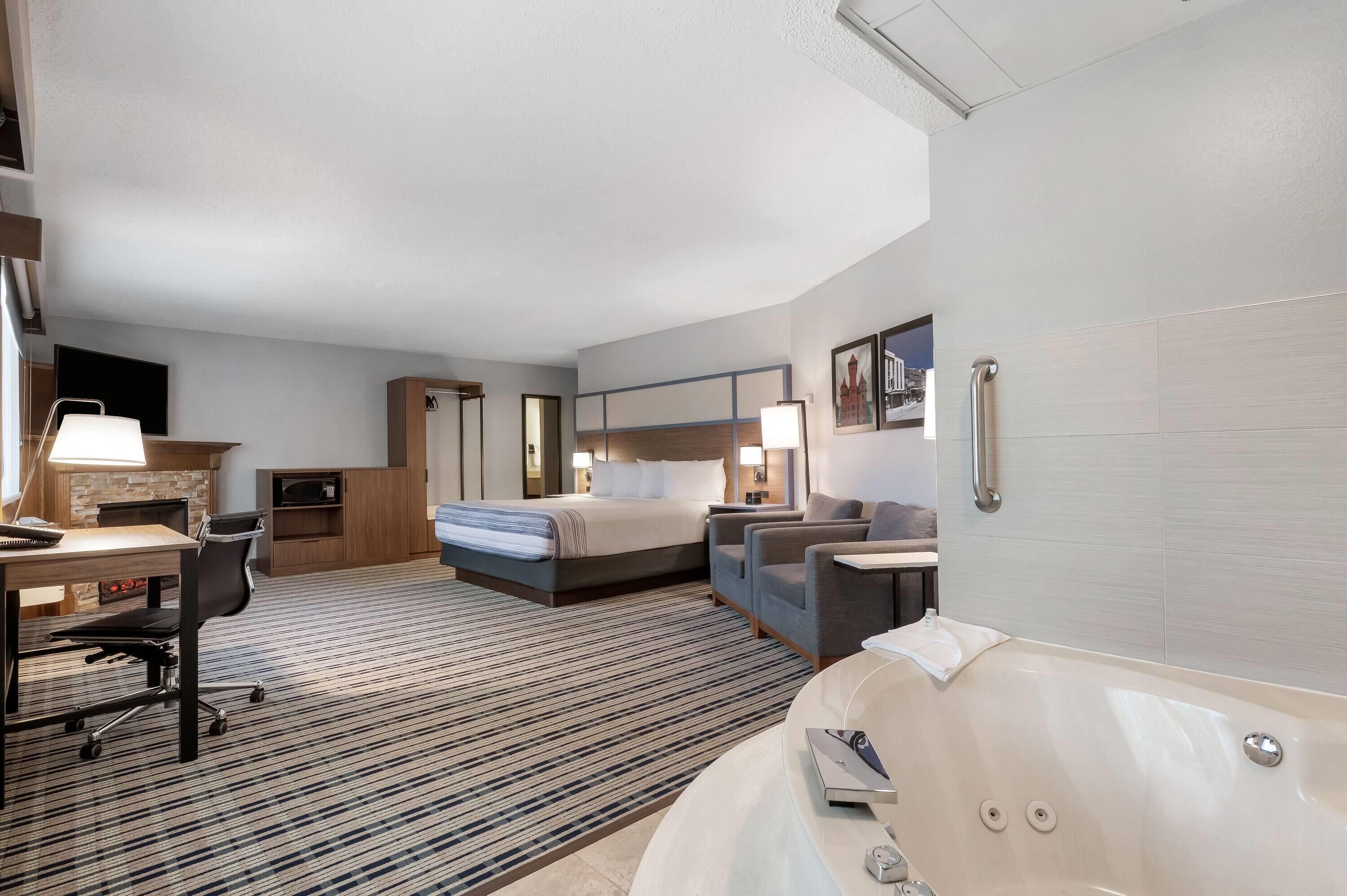 Ett hotellrum med en säng, ett skrivbord, en stol, en soffa, ett badkar och en TV.