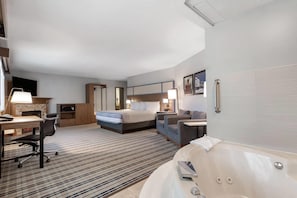 A hotel room with a bed, a desk, a chair, a sofa, a bathtub, and a TV. - AmericInn by Wyndham Fergus Falls - Conference Center (Fergus Falls)