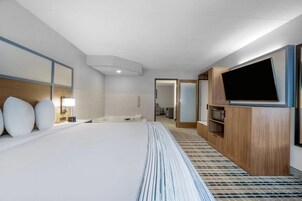 Habitación de hotel con una cama grande, televisión, microondas y baño visible a través de una puerta abierta.
