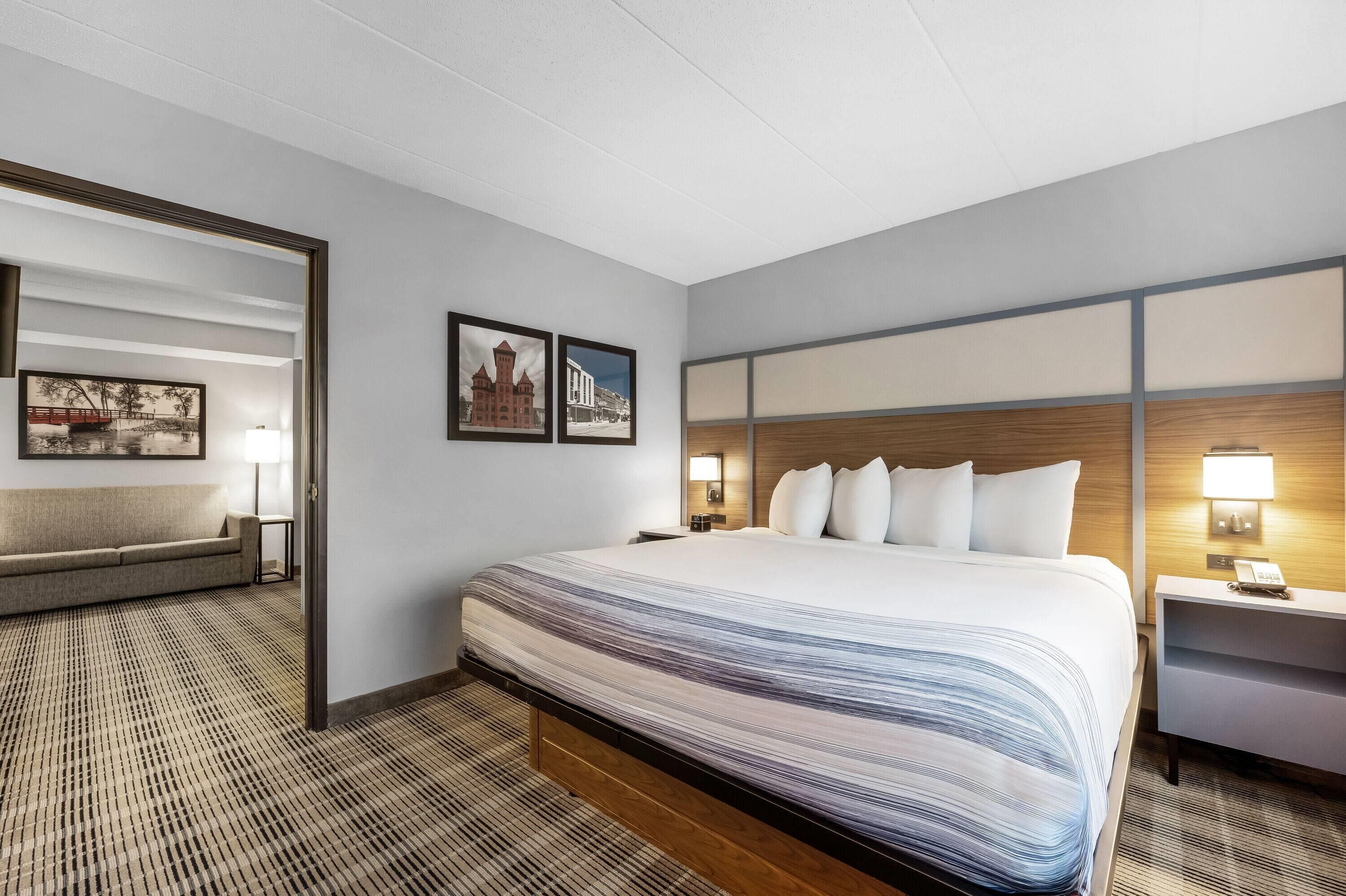 Ett hotellrum med en stor säng, ett nattduksbord, ett skrivbord, en stol och två inramade tavlor på väggen.