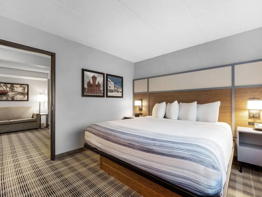 Ett hotellrum med en stor säng, ett nattduksbord, ett skrivbord, en stol och två inramade tavlor på väggen.