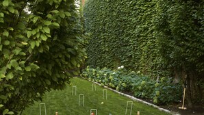 Een verzorgde tuin met een gazon, verschillende boogjes voor jeu de boules en een haag.