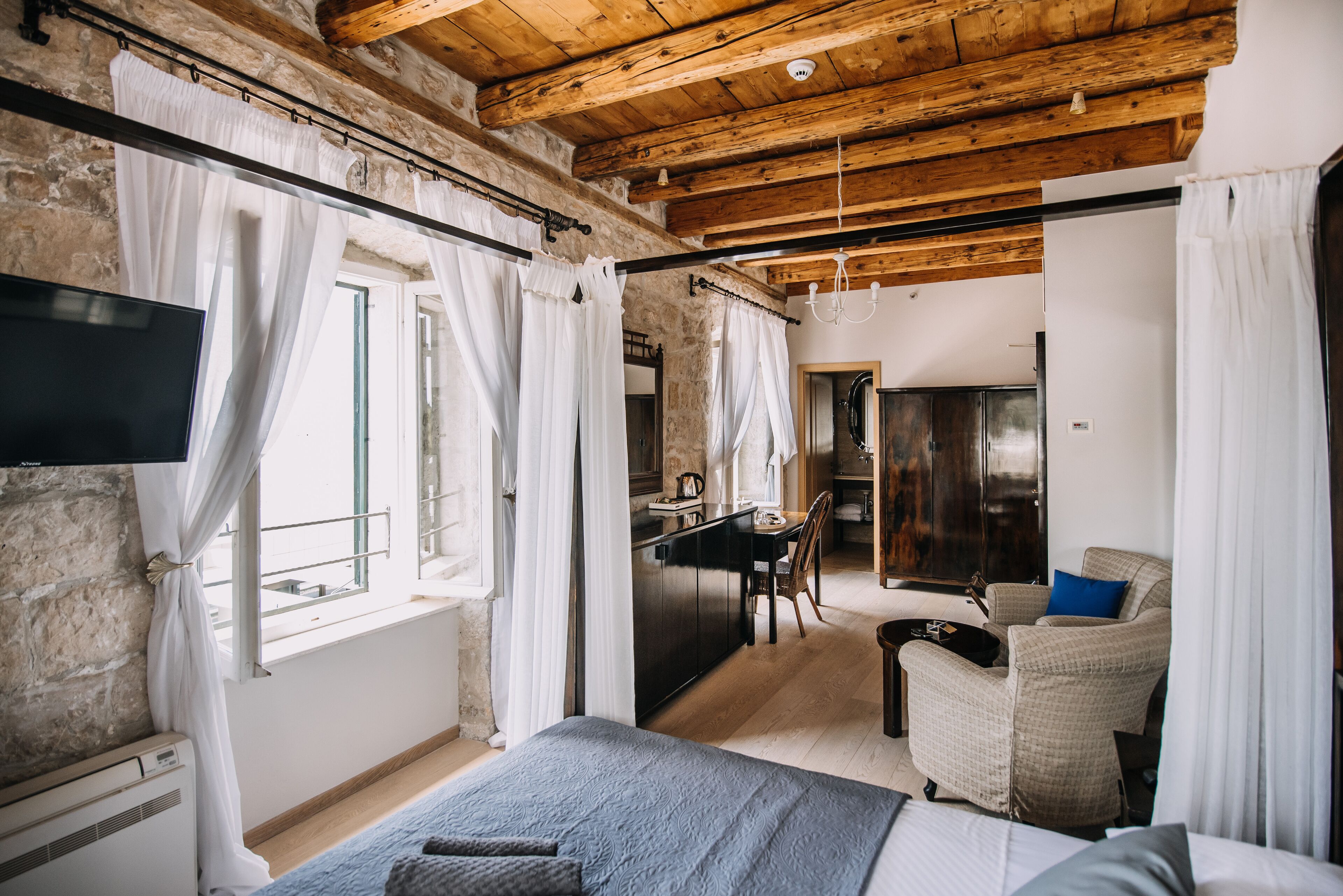A bedroom with a bed, a desk, and a chair. There is a TV mounted on the wall.