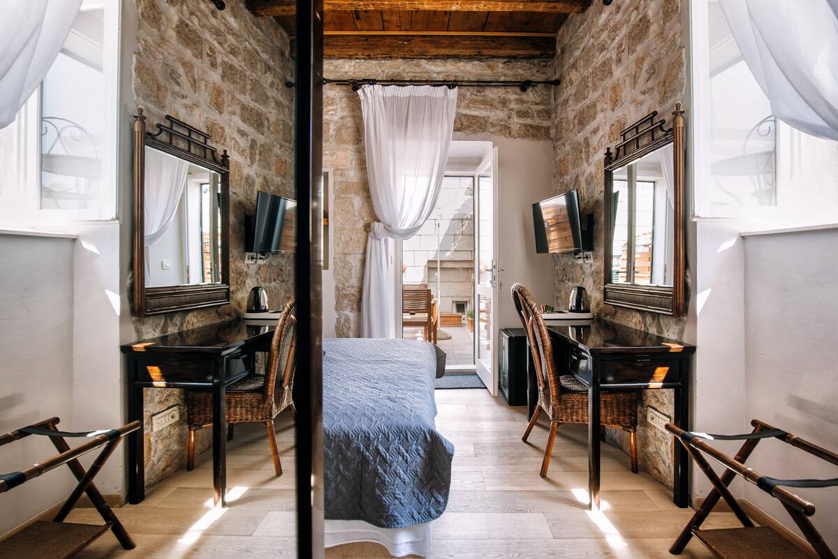 Een slaapkamer met een bed, twee bureaus, twee stoelen, een televisie en een grote spiegel.