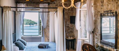 Un dormitorio con cama, una silla, una mesa, una araña y vistas al mar.