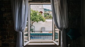 Una ventana con cortinas blancas, vista a un balcón con barandilla azul y un muro de ladrillo.