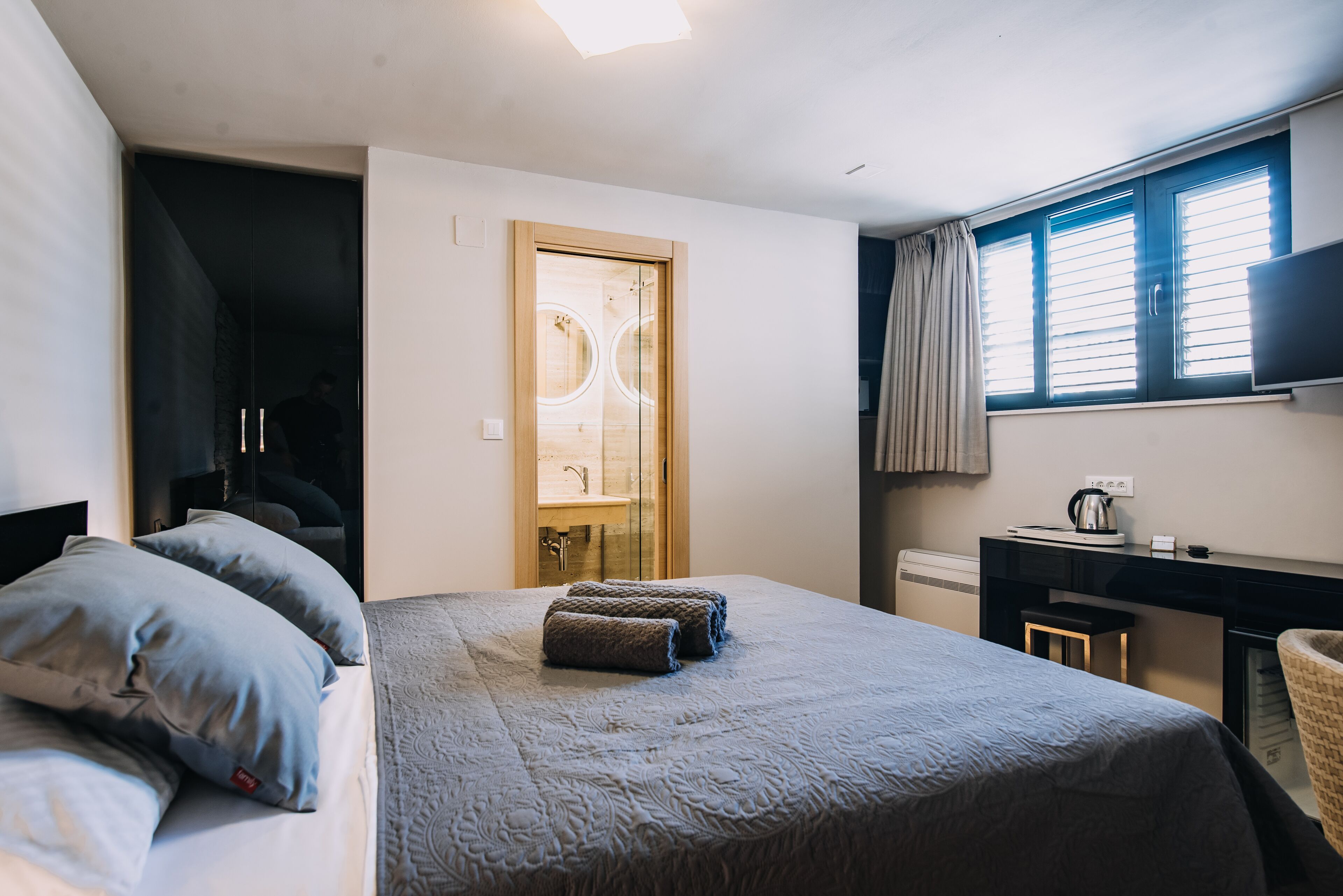 Ein Hotelzimmer mit einem Bett, einem Schreibtisch, einem Sessel, einem Fernseher und einem Vorhangfenster.